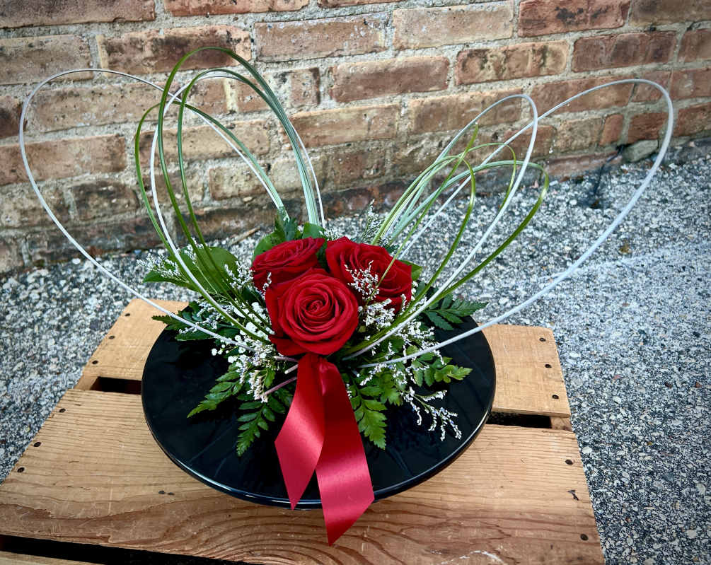 A low black dish with red roses nestled in filler flowers and