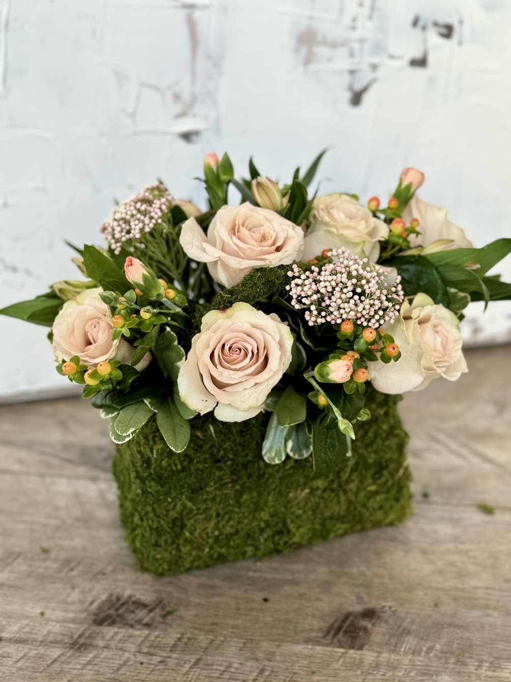 Crafted within a charming moss purse, this floral arrangement exudes grace and