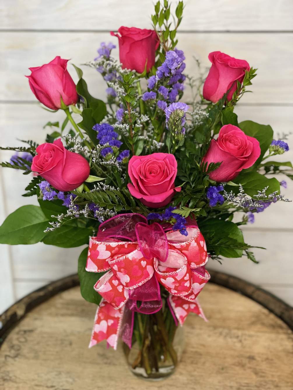 6 hot pink roses with filler flower arranged in a vase. Hot