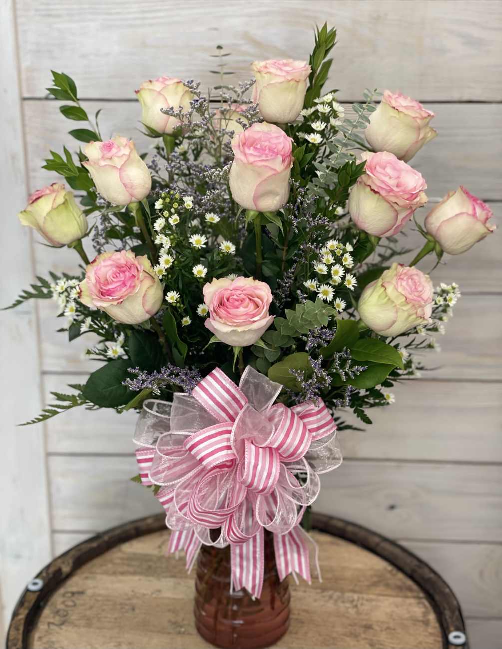 A dozen pink roses arranged in a vase with filler flowers and