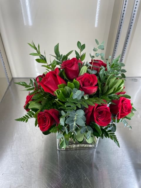 Red roses with mixed greens in a glass vase.