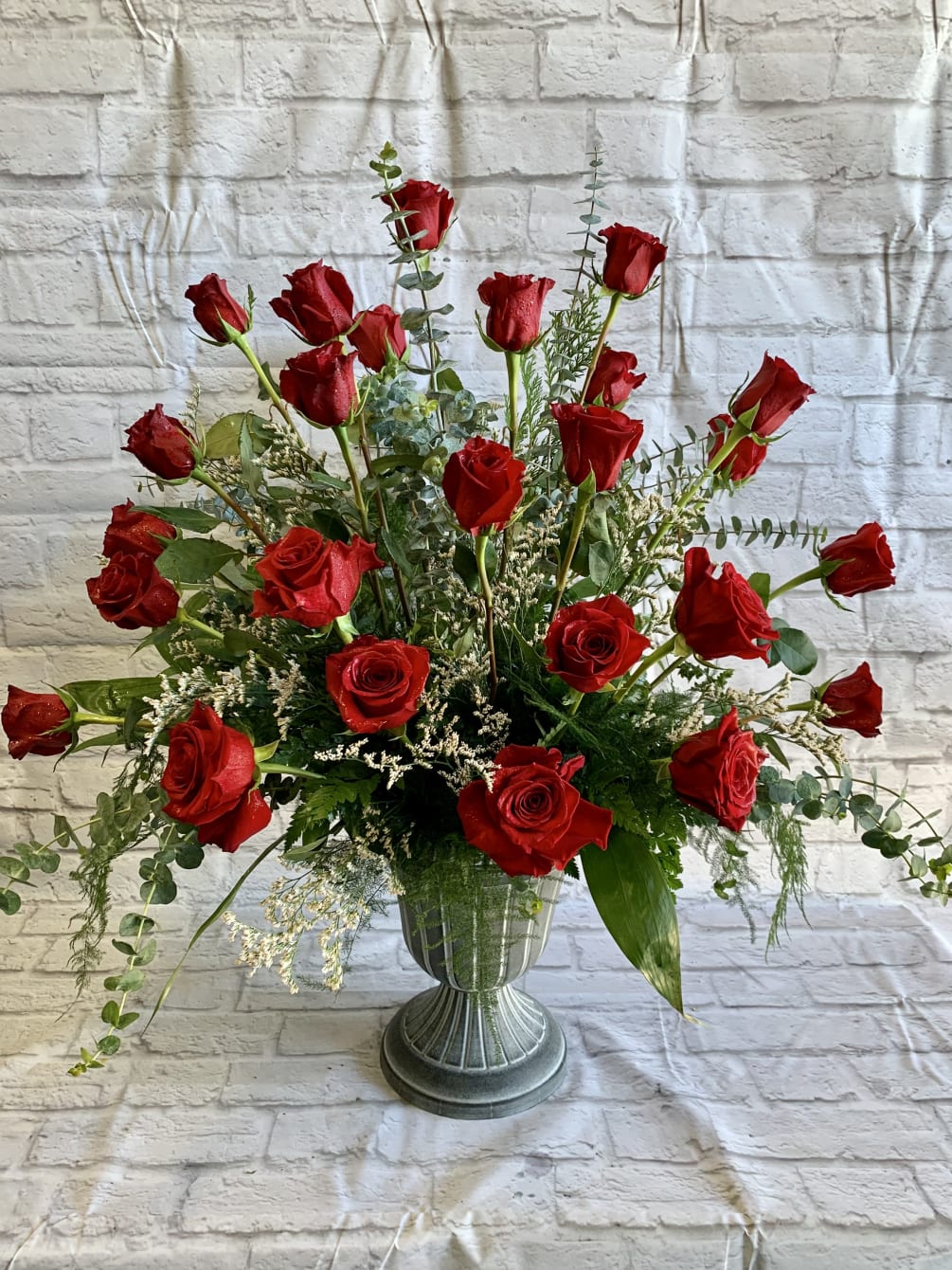 24 Beautiful red roses displayed in an urn accented with a mixture