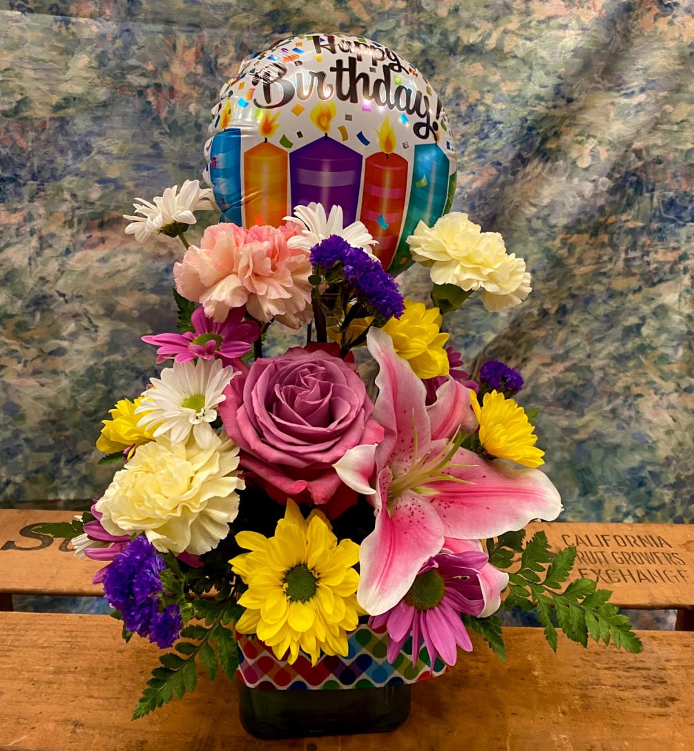 A glass cube filled with colorful blooms and a small Happy Birthday