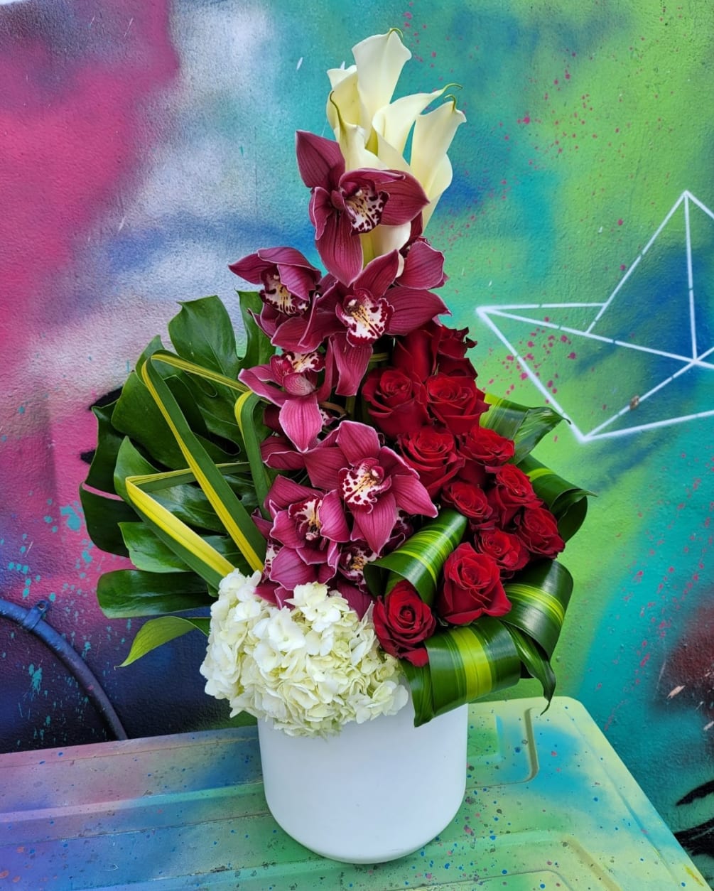 An arrangement in a vase, with roses, hydrangeas, Callas, cymbidium, and greenery.