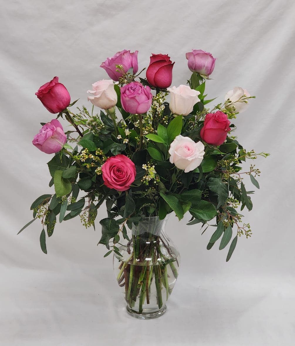 A vase full of a dozen roses in various shades of pink