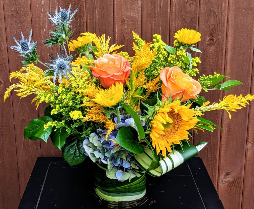 Golden blooms and orange roses are complimented with blue thistles and hydrangea.