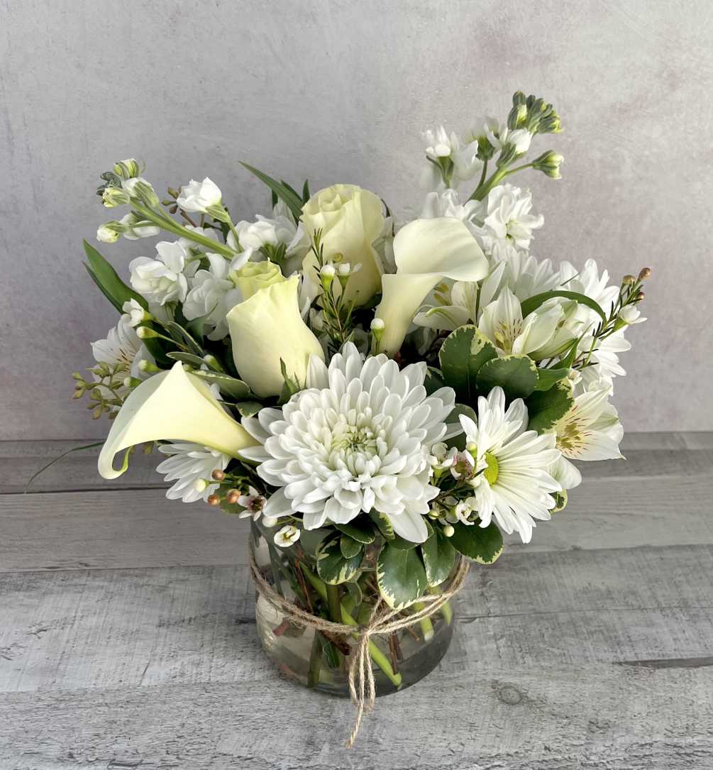 A clear glass cylinder with white stock, white calla lilies, roses, white