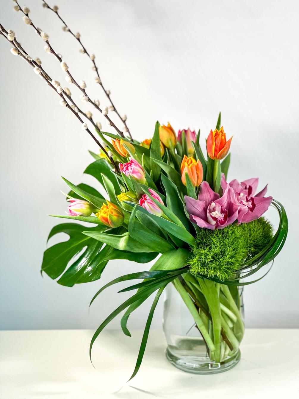 Playful combination of Tulips, Green Trick, and Cymbidium Orchid in a glass