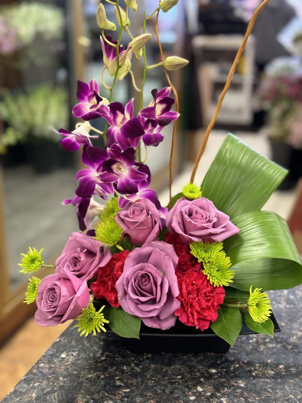 Modern, tropical design of dendrobium orchids, lavender roses, hot pink carnations, green
