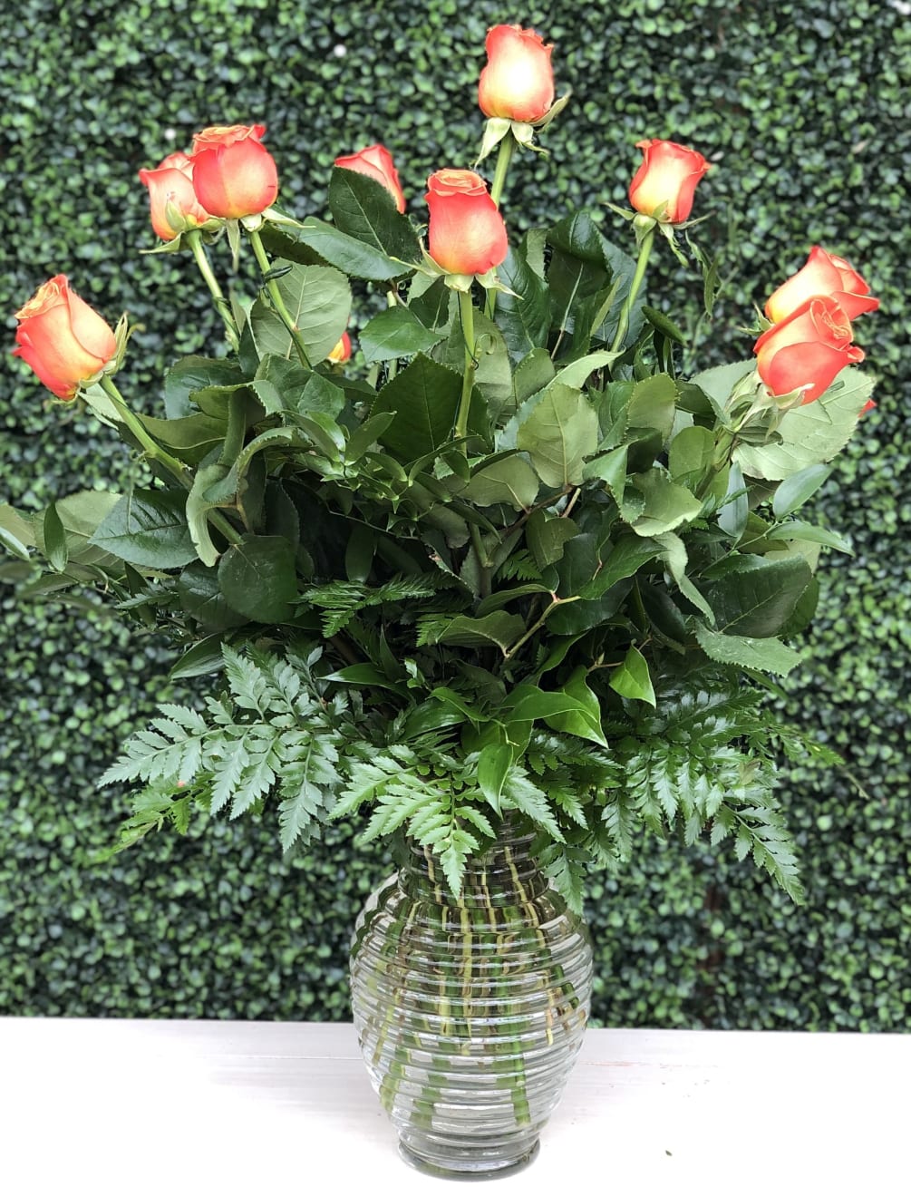 A traditional arrangement of orange roses and greens in a glass vase.