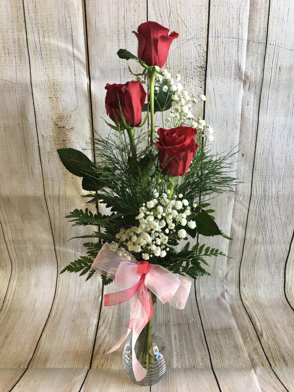 3 beautiful red roses arranged in a glass vase with filler &amp;