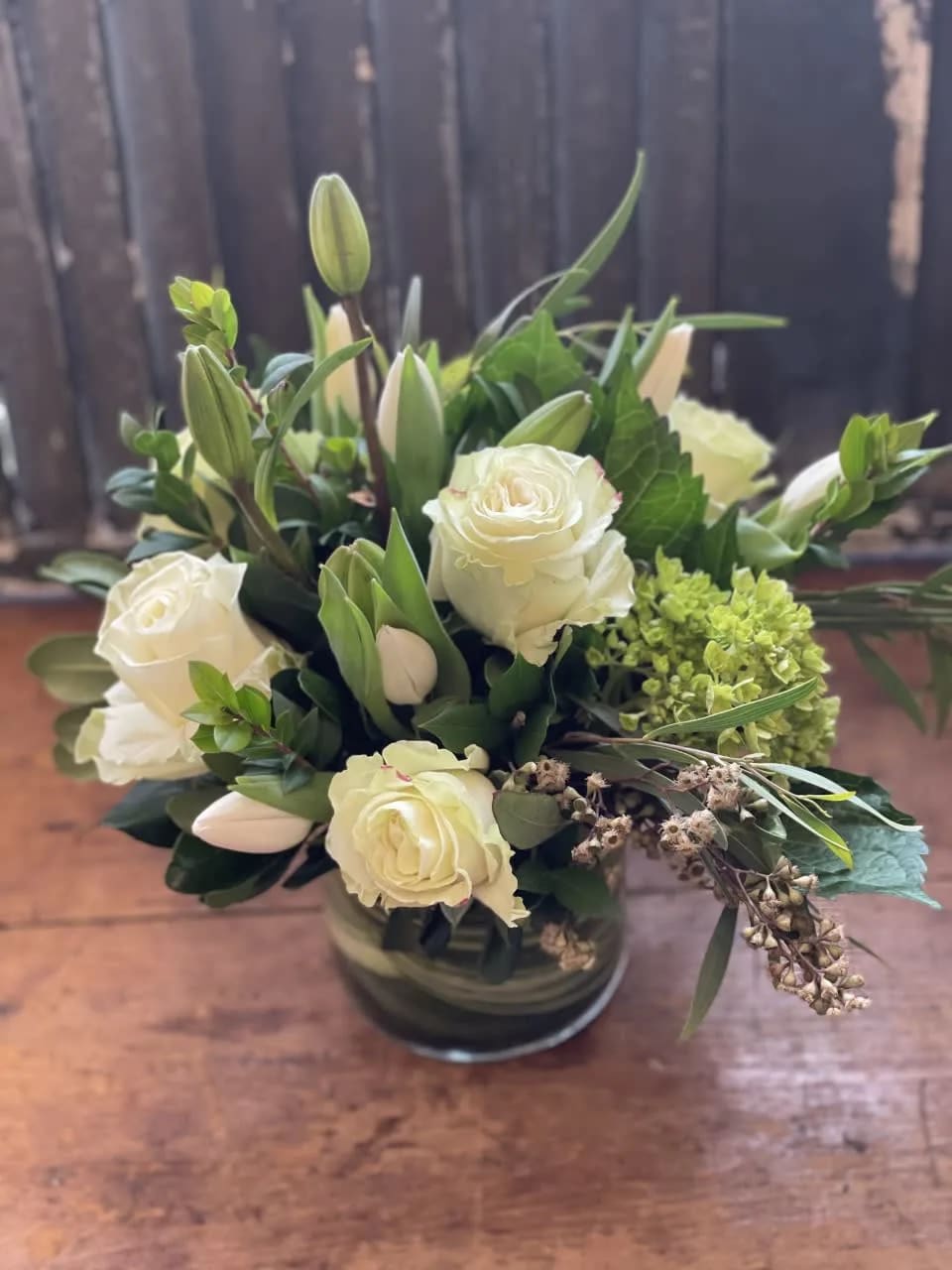 A variety of green and white flowers in a short clear vase.