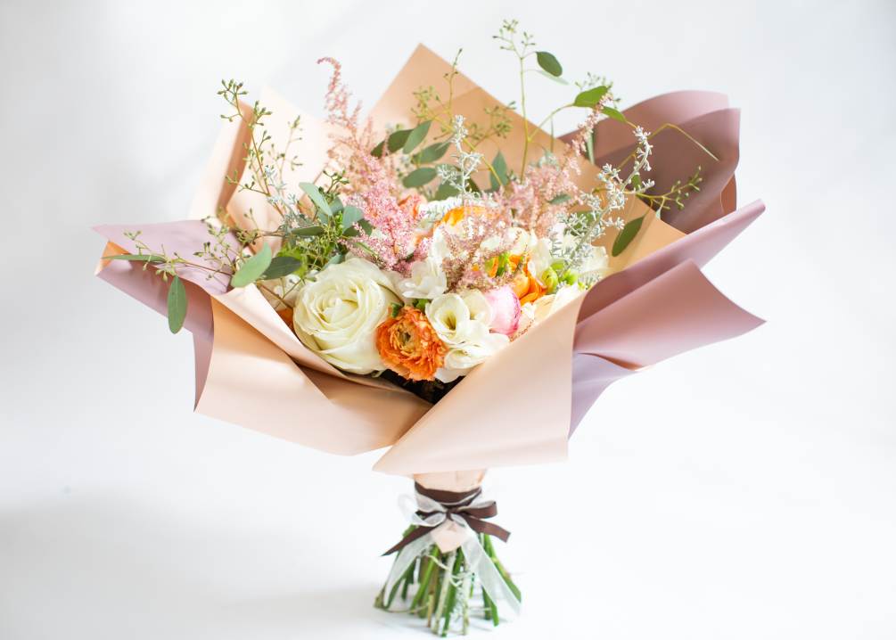 A hand-tied arrangement includes roses, hydrangeas, freesias, and ranunculus.