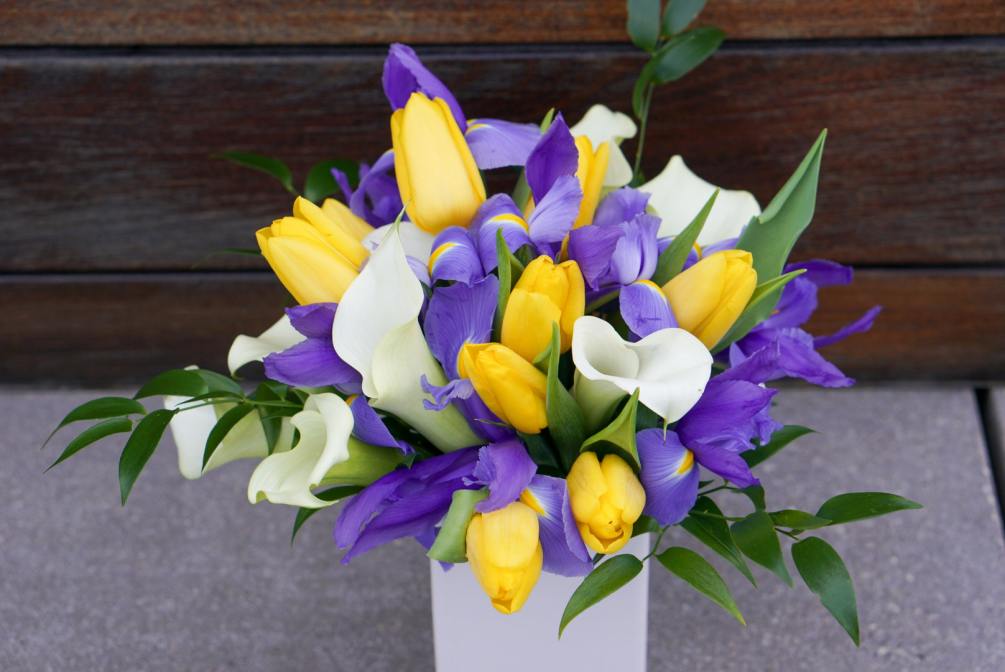 A vase arrangement contains tulips, irises, calla lilies, etc