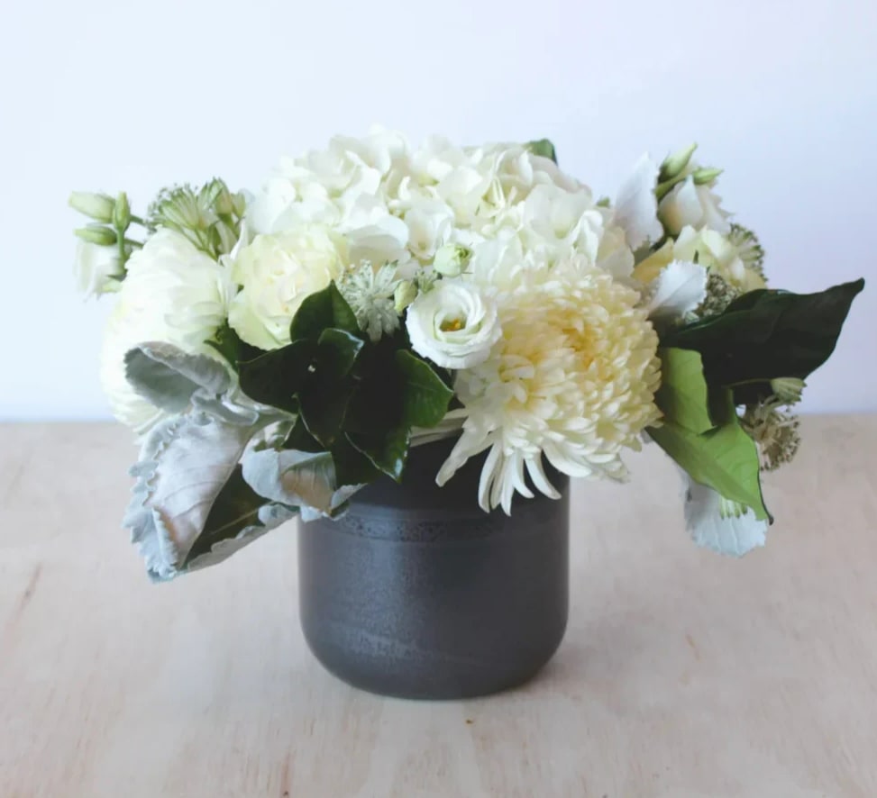 A petite all white arrangement with hydrangeas, roses, lisianthus, and blooms in