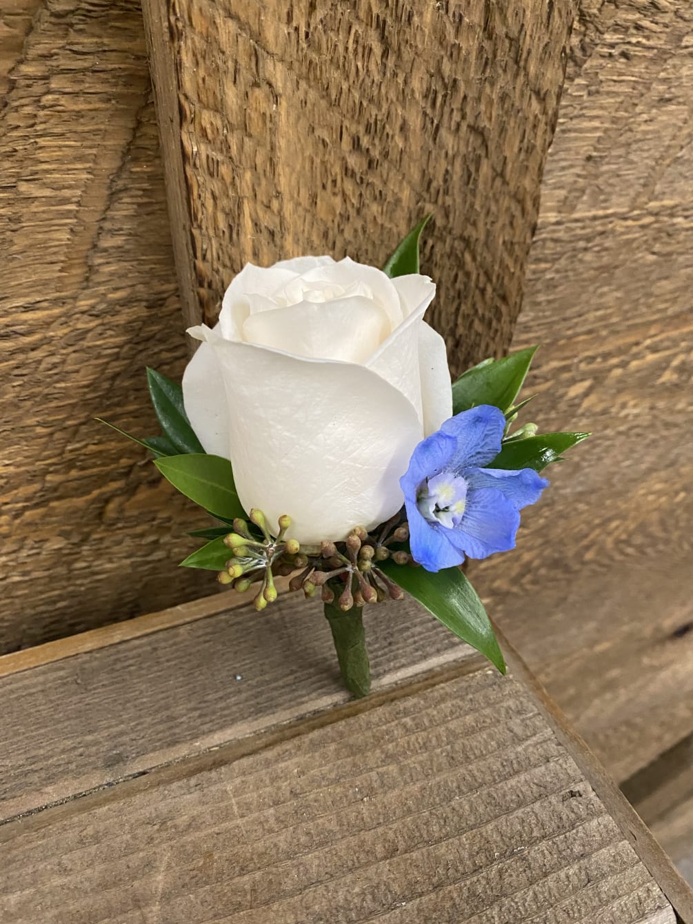A beautiful white rose boutonniere accented with light blue delphinium. 
