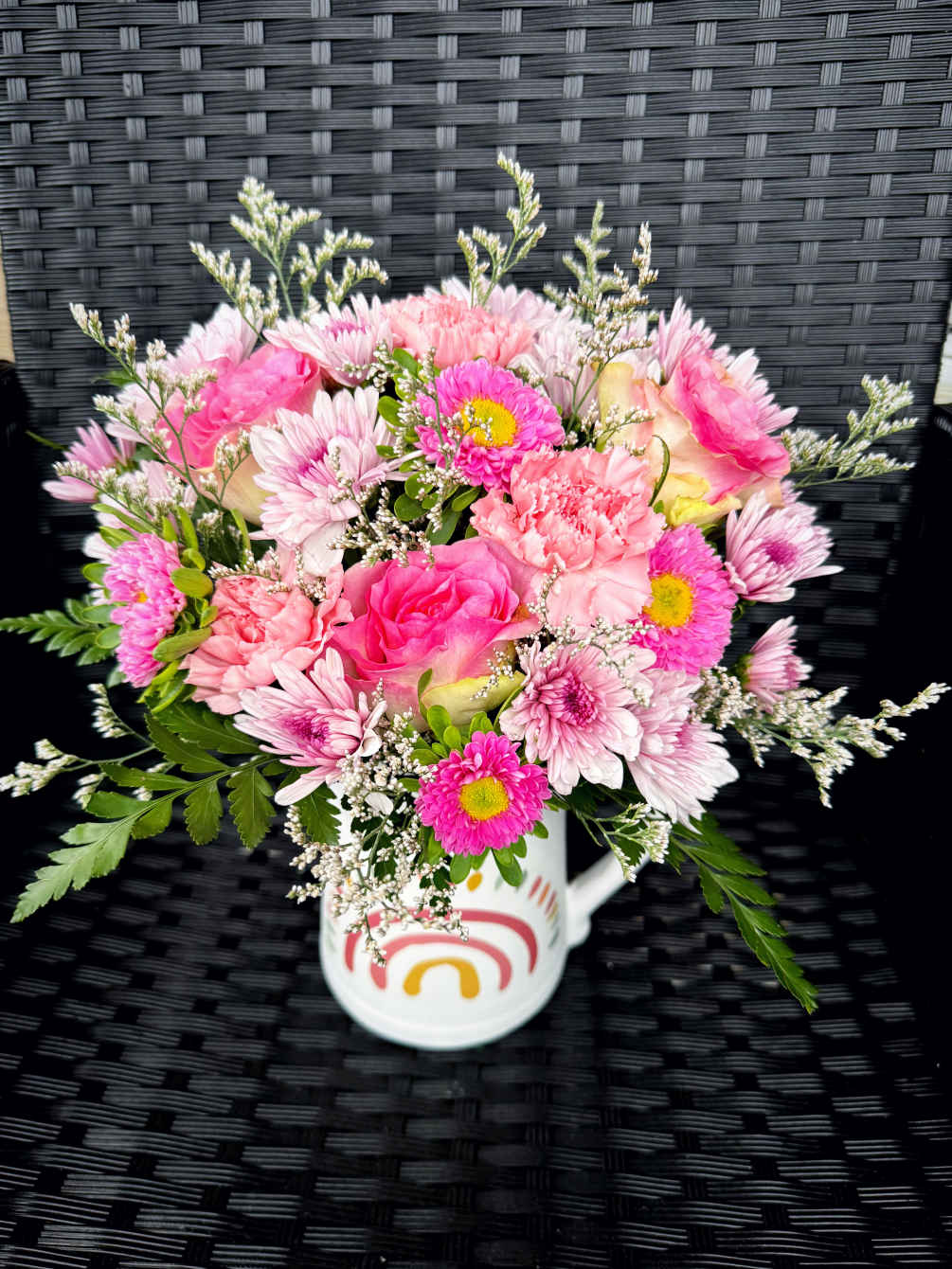 Spring mixed flower arrangement in a pitcher in pink colors. 