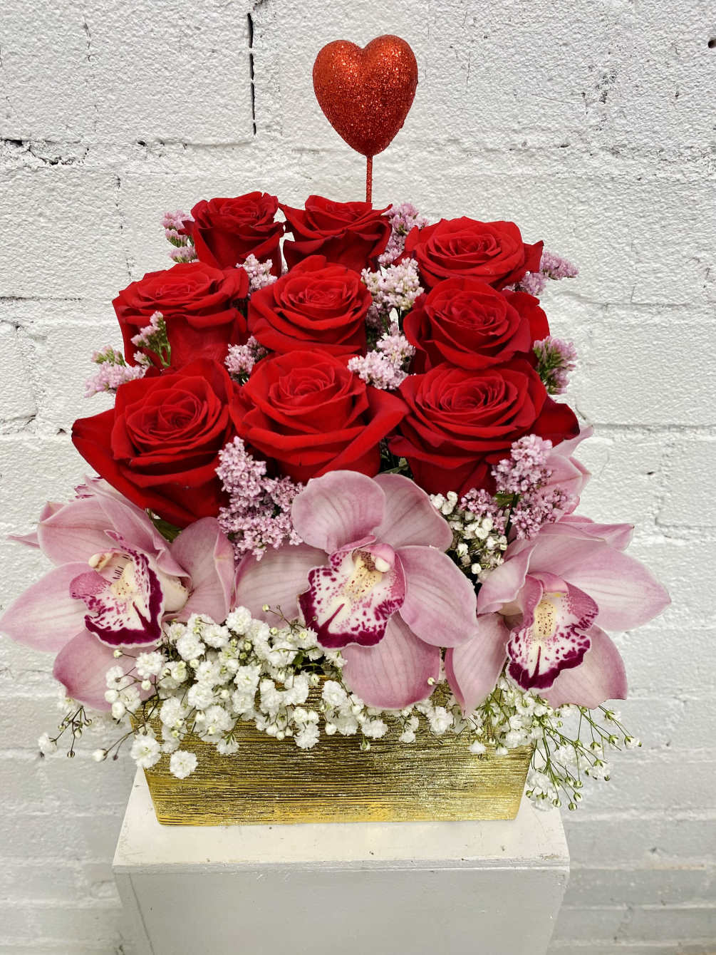 Romantic red roses and pink cymbidium orchids in a brushed golden box.