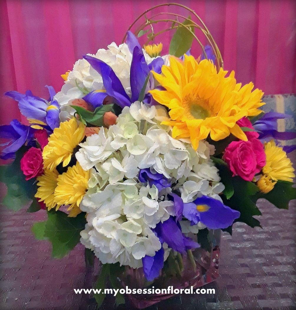 Ireses, hydrangea, roses, spray roses, and daisies, arranged compact in cube glass
