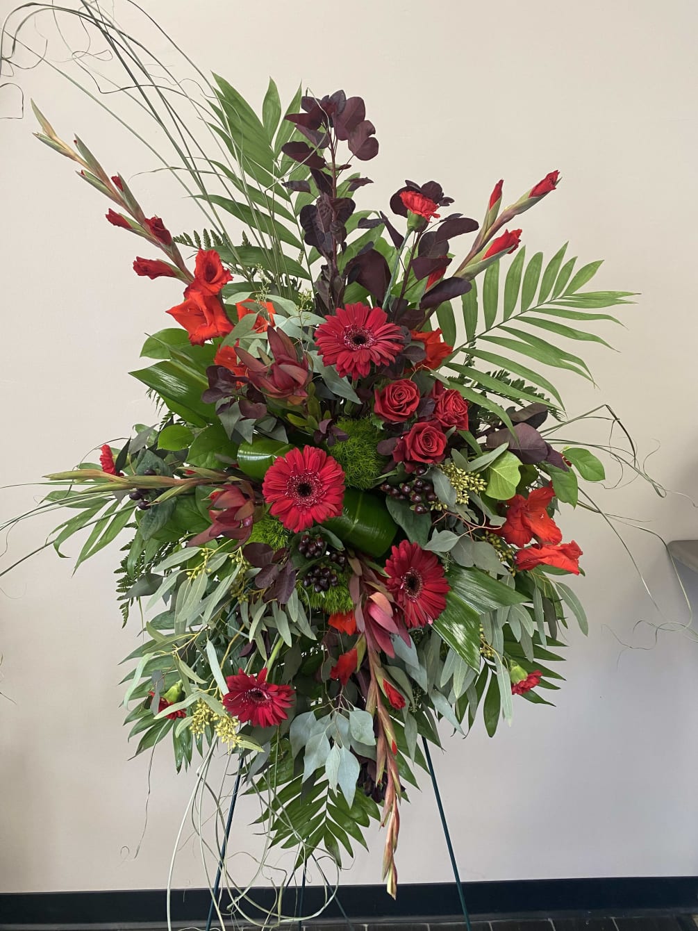 A standing spray in rich red florals for a respectful farewell. 