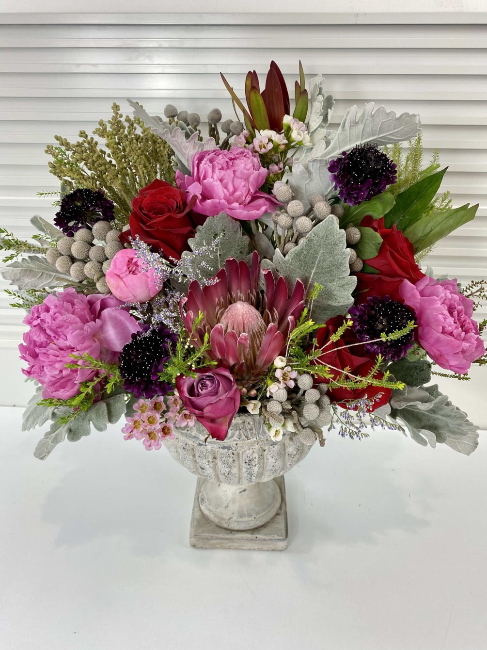 Elegant one-sided flower arrangement with peonies, roses, protea and wax flower surrounded