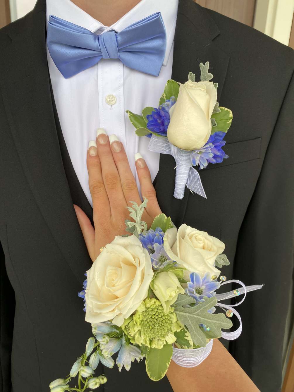 Elegant white roses with blue delphiniums and mixed greens. This is a