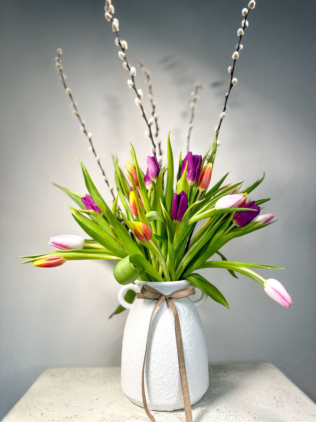 The mix of colorful tulips in a ceramic two-handled jar creates a