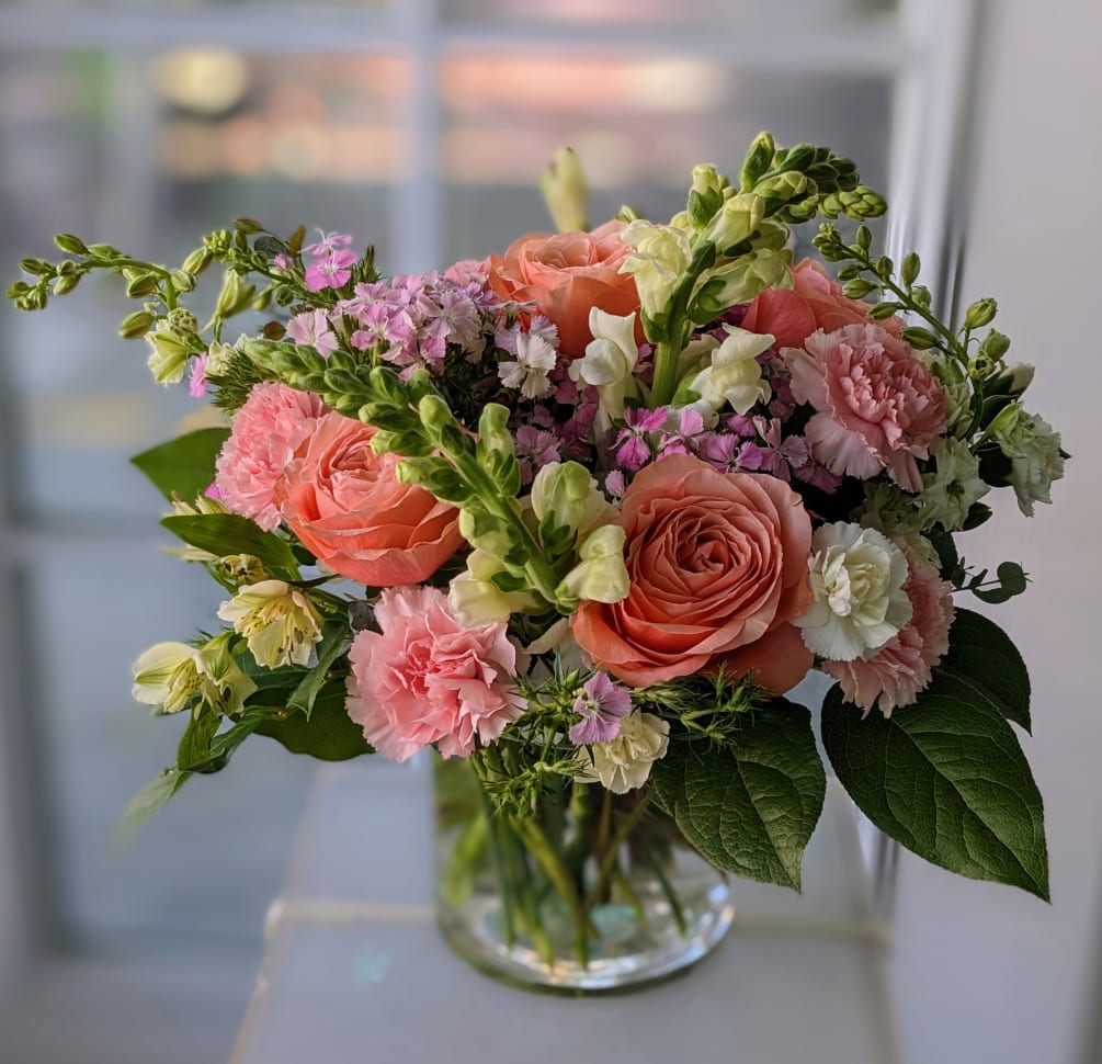 Peach, white, and blush pink colored flowers in a low cylinder vase.