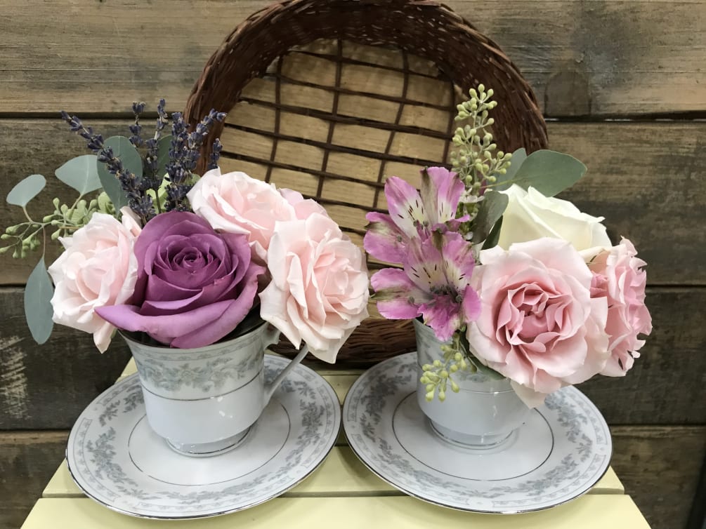 Two lovely tea cups filled with seasonal flowers and greens, presented in