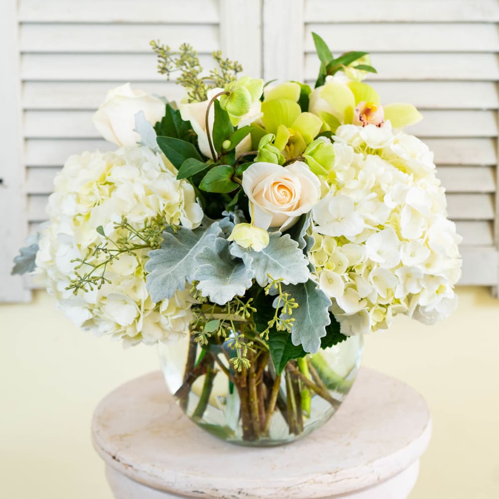 A bubble bowl filled with hydrangea, cymbidium orchids, roses, hypericum berries, dusty