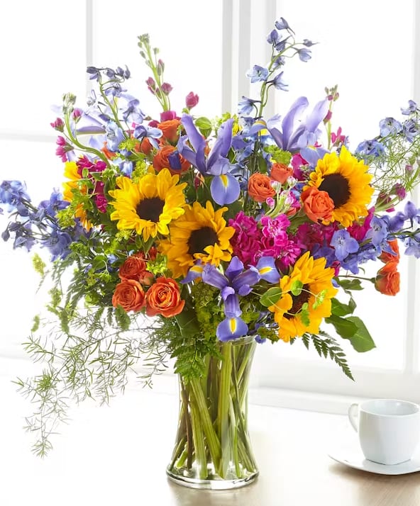 Joyful and colorful, this bouquet includes delphinium, sunflowers, iris, stock, spray roses