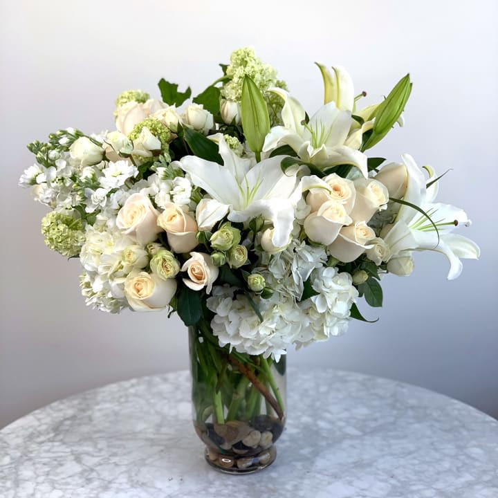 A glass vase with lilies, roses and hydrangeas.