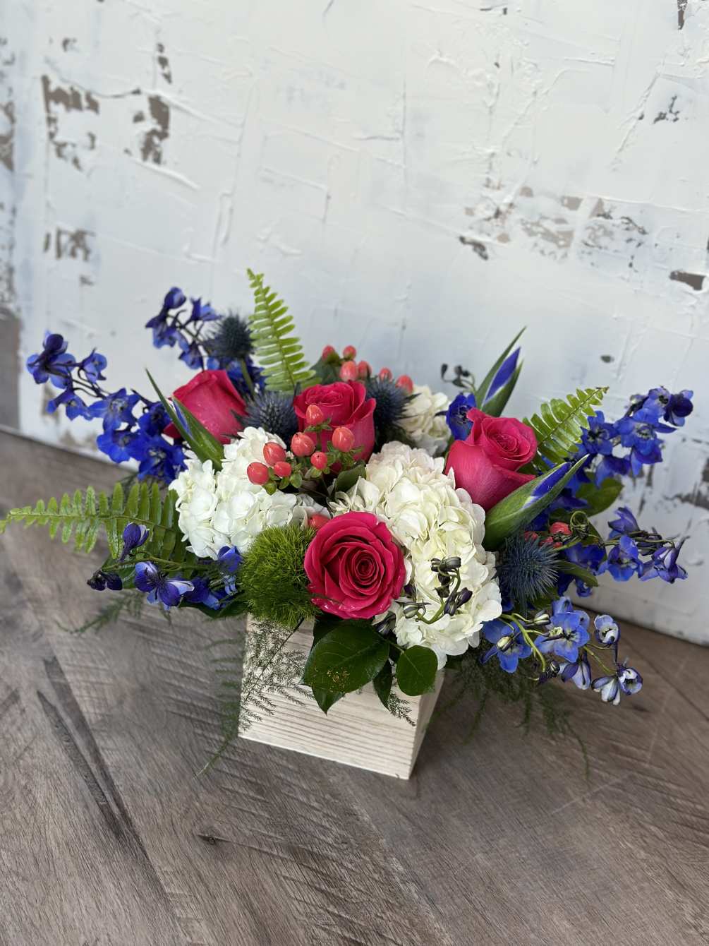 Cabana Flower arrangement features hot pink roses, blue delphinium and white hydrangeas.