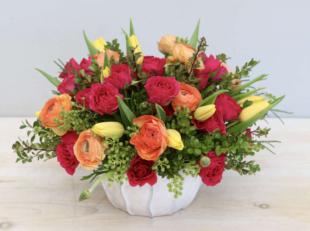 This joyful arrangement is made with bright pink spray roses, orange ranunculus