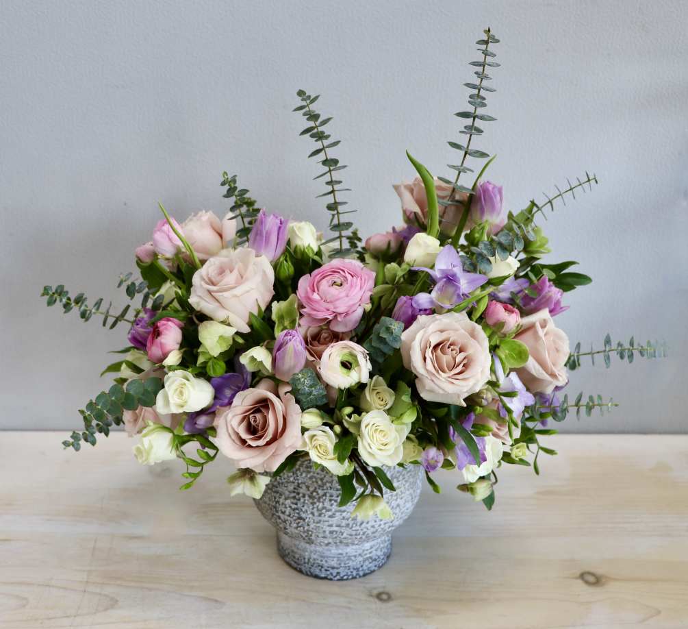 This arrangement pairs roses with ranunculus, mixed with tulips, freesia and seasonal