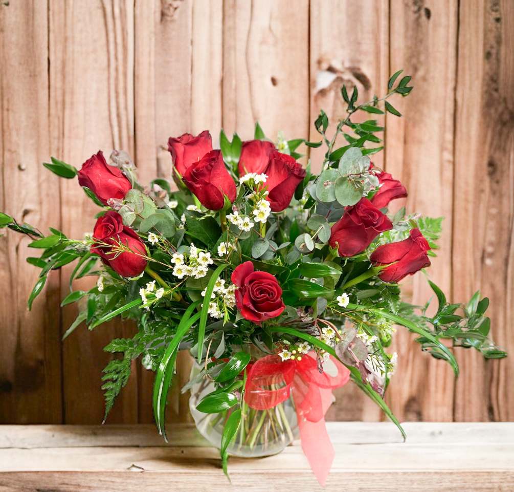 12 Red roses accented with premium greens in a tall clear vase.