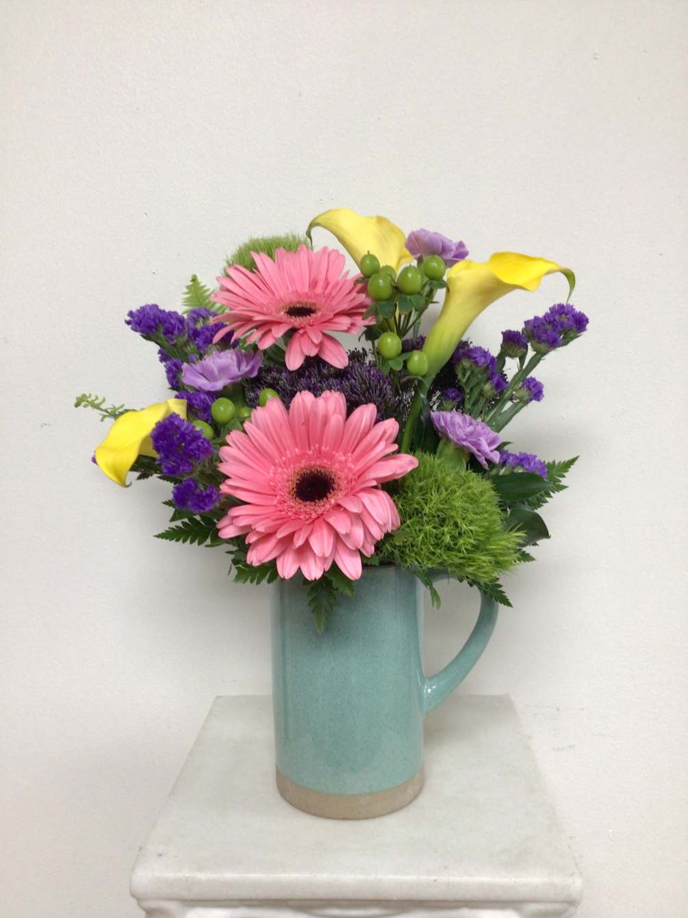 This aqua stoneware ceramic pitcher is arranged with pink gerbera daisies, purple