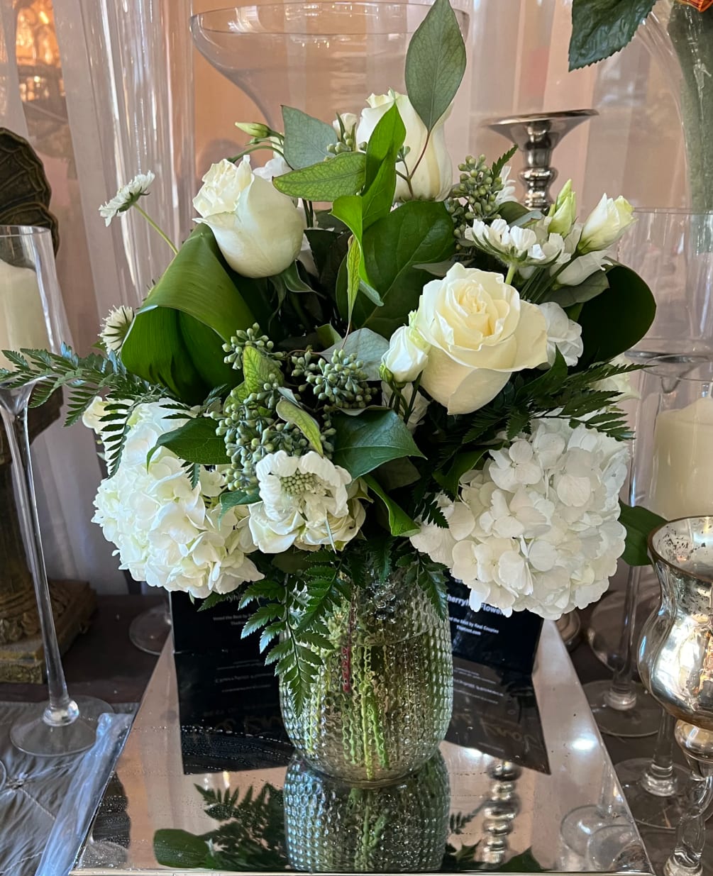 A tall clear vase with all white flowers and greenery. 

Shown in