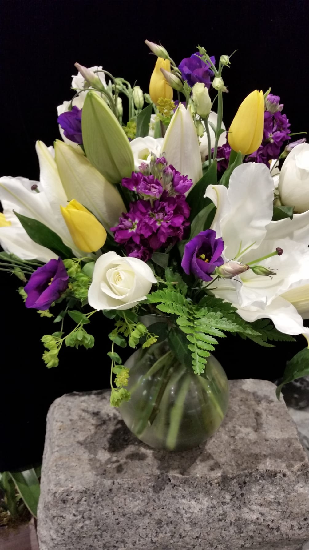 A sweetheart vase, a few white Oriental lilies, purple stock, and yellow
