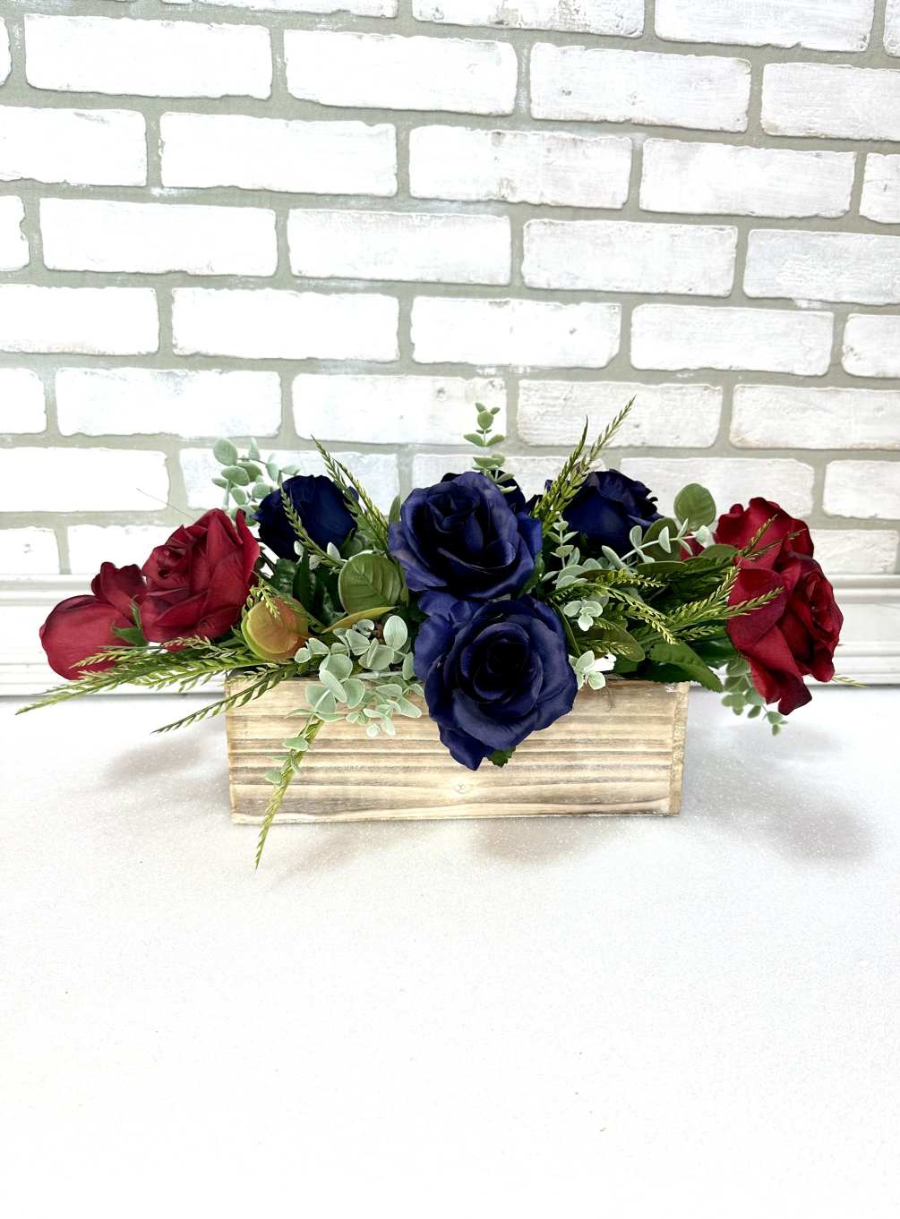 A wooden box arranged with artificial navy blue &amp; burgundy roses, and