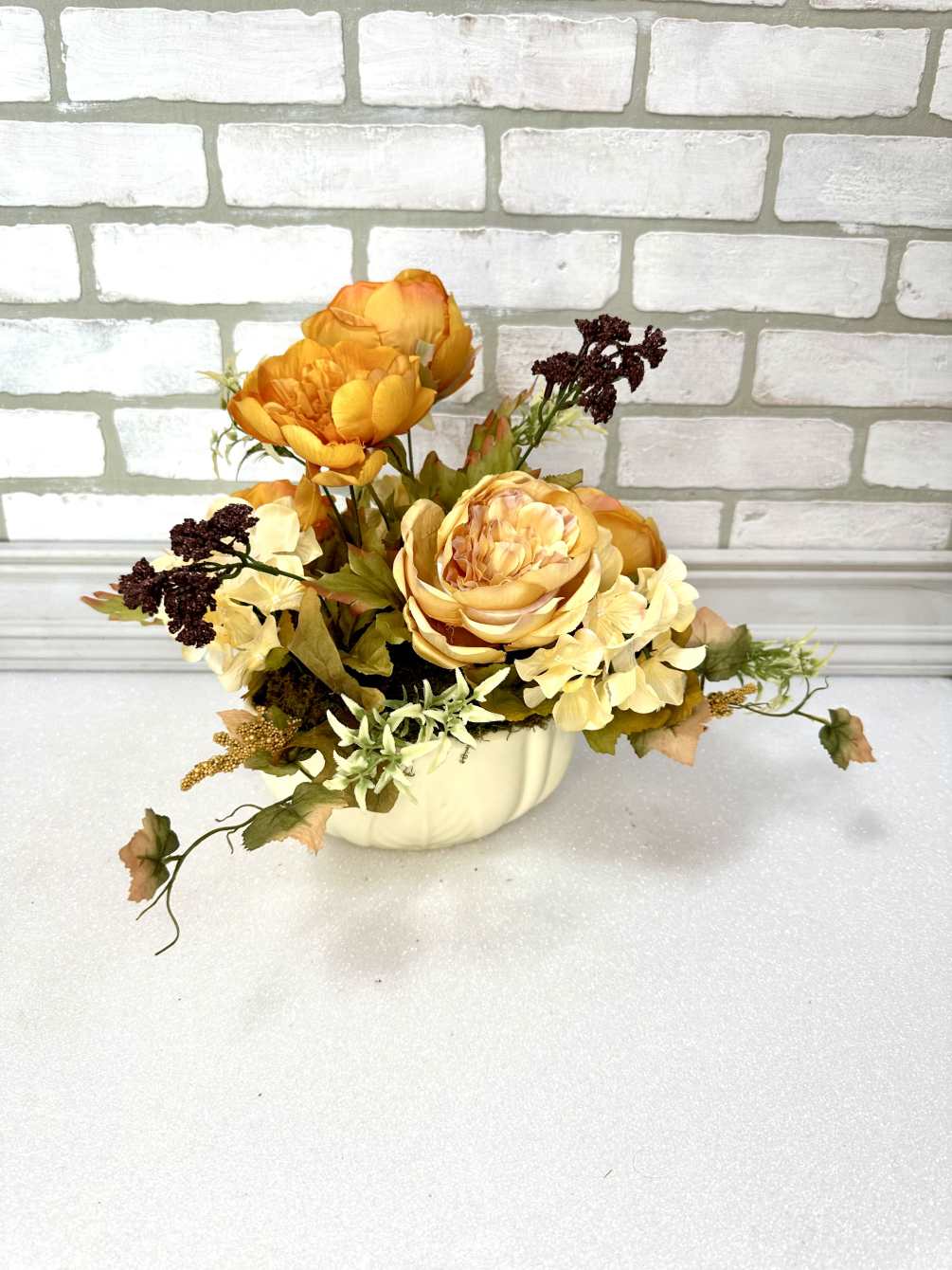 An artificial arrangement with orange peonies, other mixed flowers, and greens in