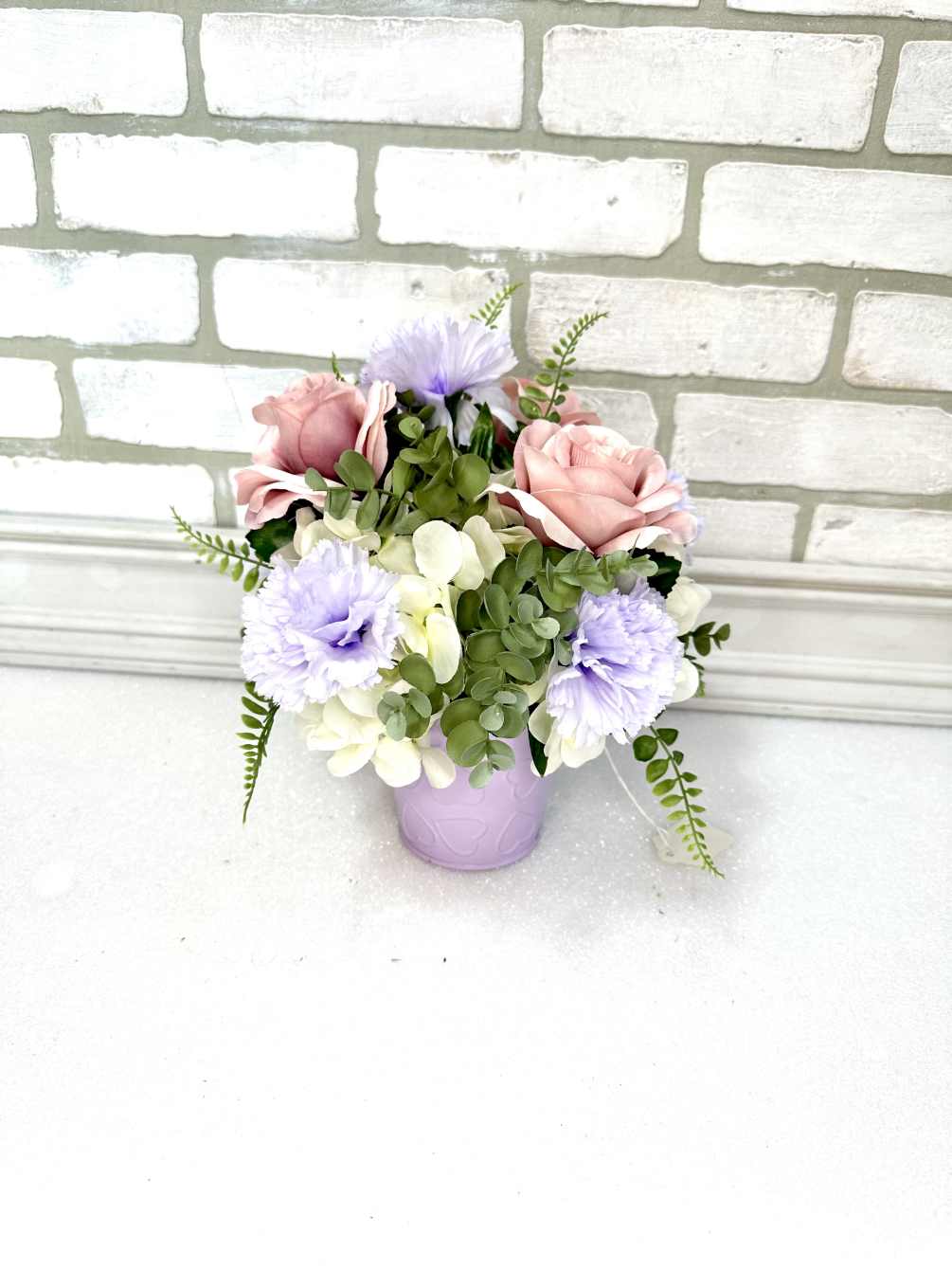 A lavender tin with hearts arranged with white hydrangea, lavender carnations, mauve