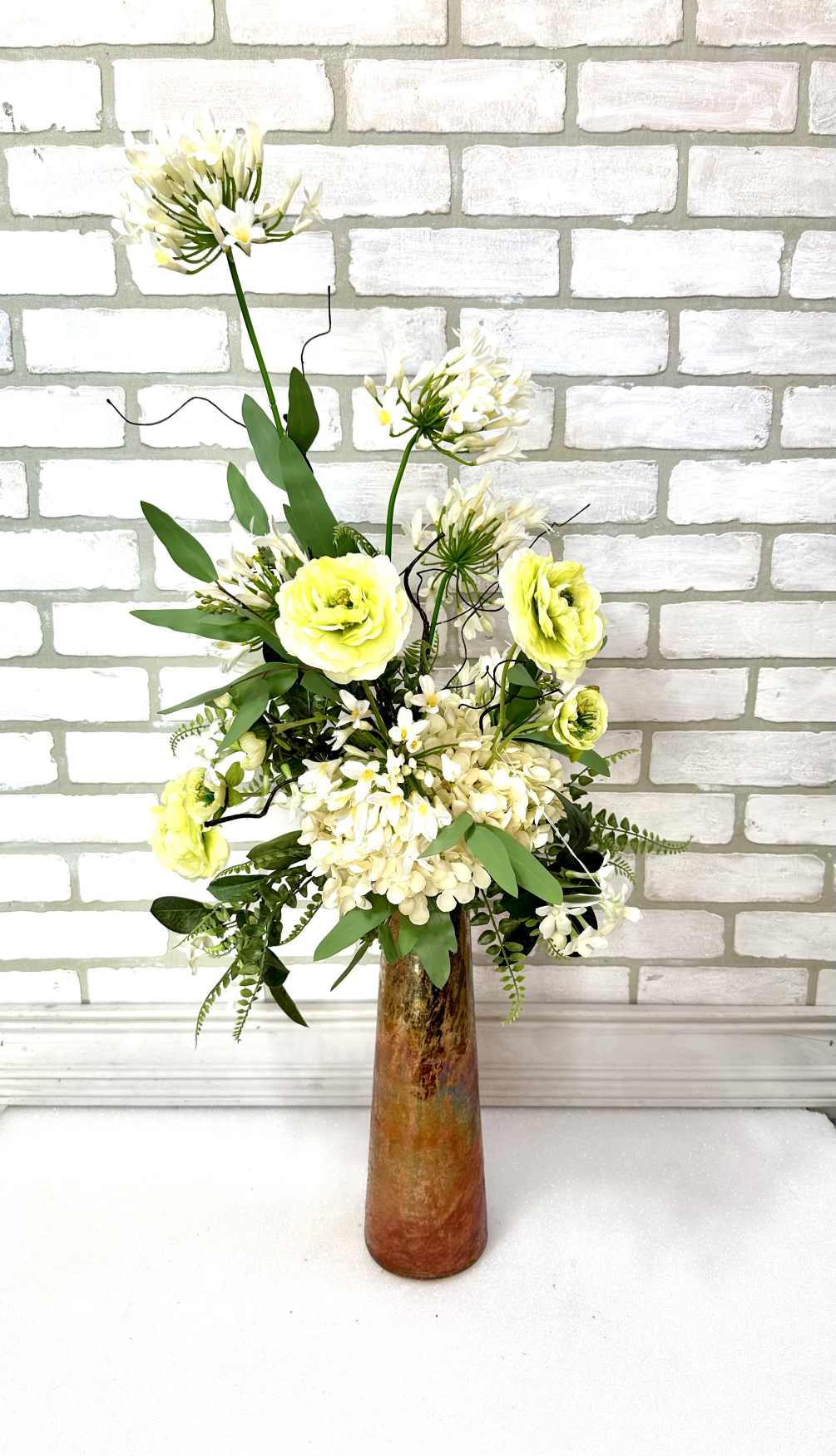 A rustic toned vase arranged with artificial white, hydrangea, two toned ranunculus