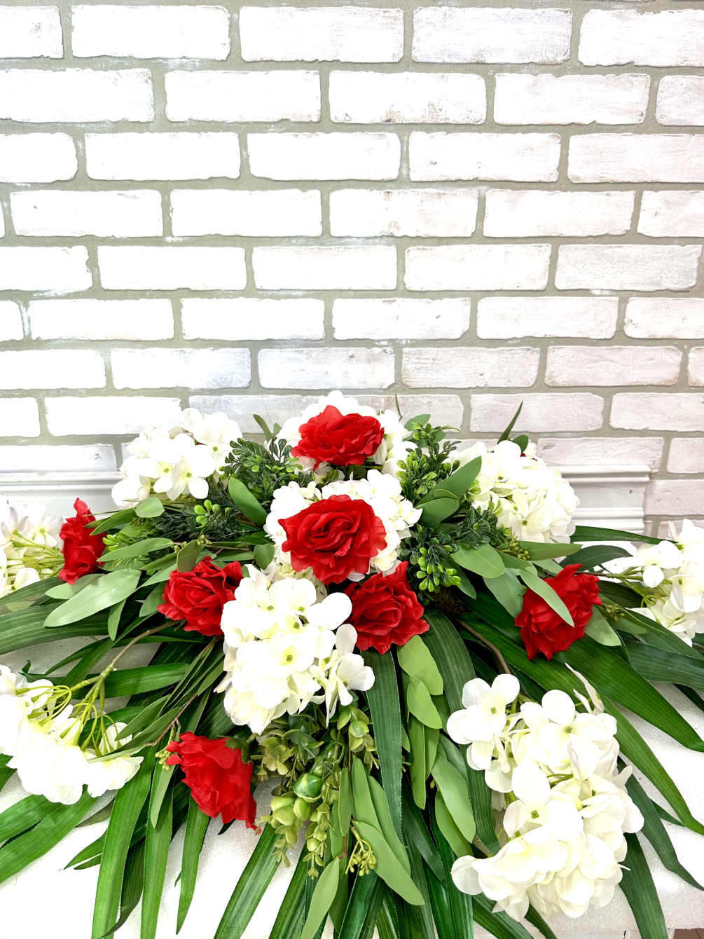 An artificial casket saddle arranged with roses, hydrangeas, and eucalyptus 
