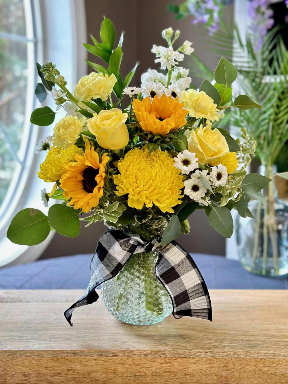 Fresh flowers include; sunflowers, roses, stock, mums, carnations with mixed greenery throughout.