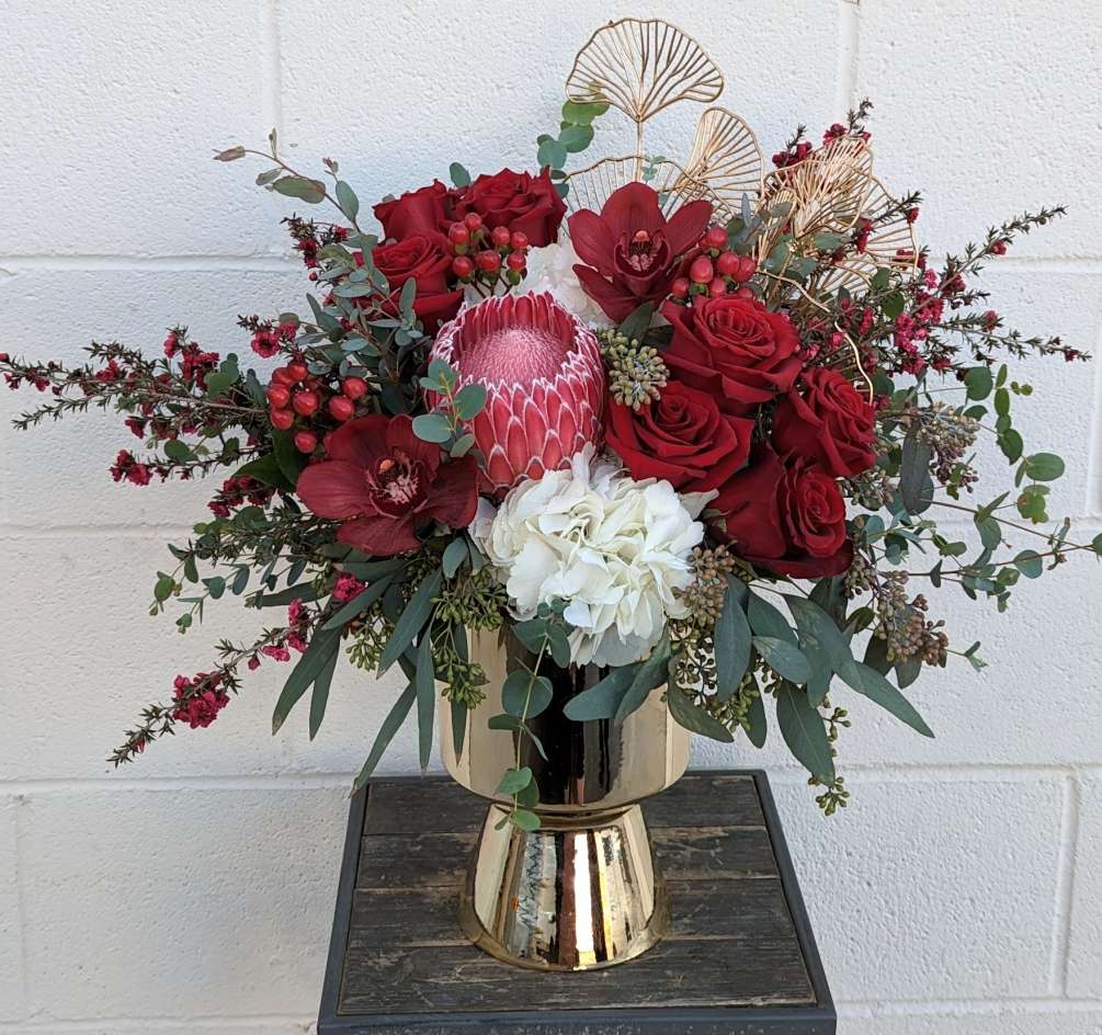 Red roses, hydrangea, protea, and cymbidium orchids in a footed gold compote.