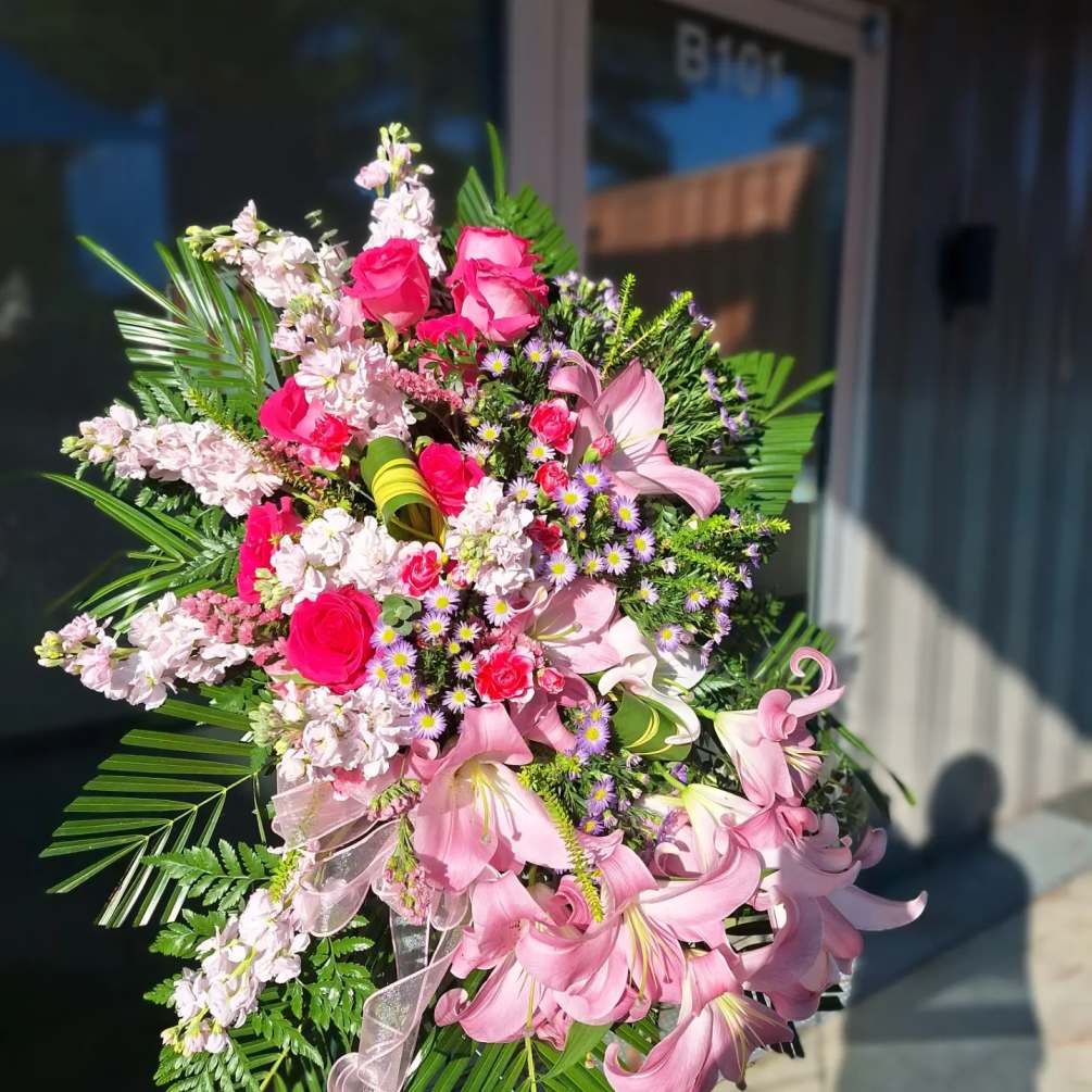 A tribute in pink with hot pink Roses, stock and Lilies arranged