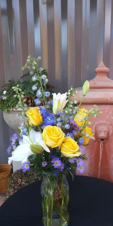 An arrangement of yellow roses, delphinium, white lilies, monte casino, greenery and