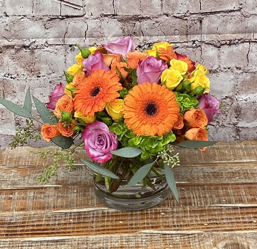 Colorful spray roses and Gerbera daisies in cylindrical vase. 