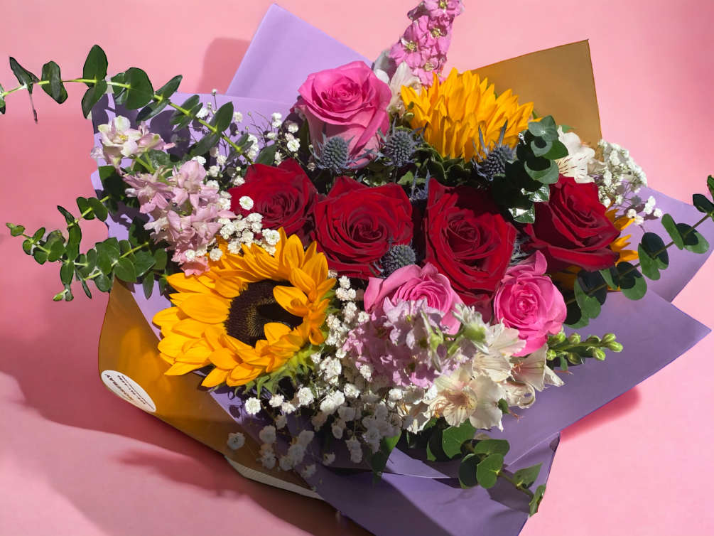 A bouquet of red and pink roses, sunflowers and other seasonal flowers